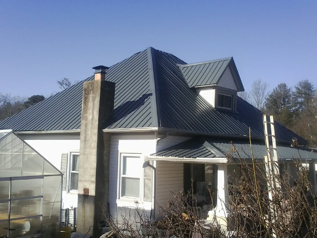 Dark blue standing seam metal roof on a white farmhouse with dormer — Slate & Tile Roof Repair by Roofing Brothers in Whitefish