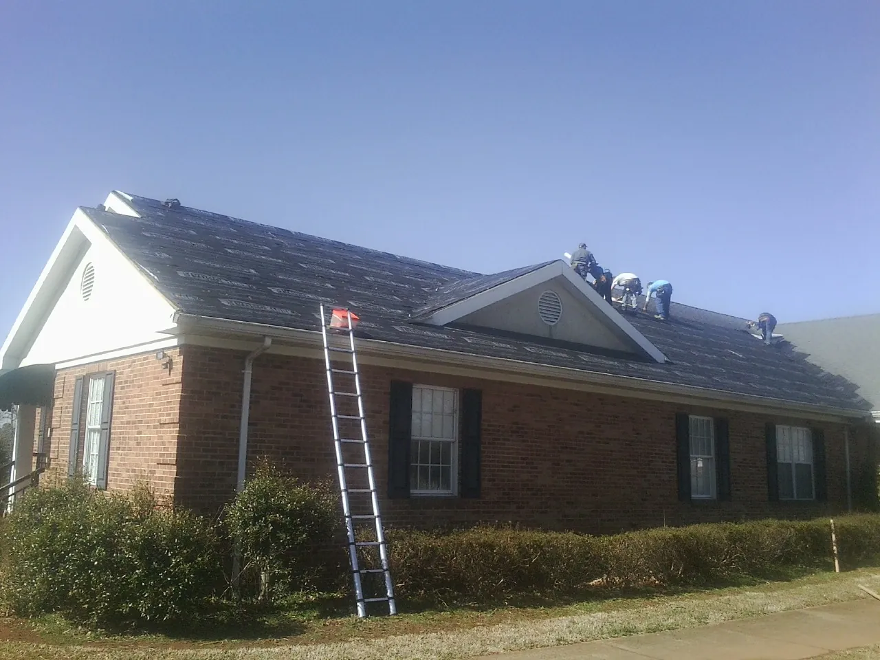 Crew tearing shingles off a brick ranch roof with a ladder set — Emergency Roof Repair work by our crew in Whitefish