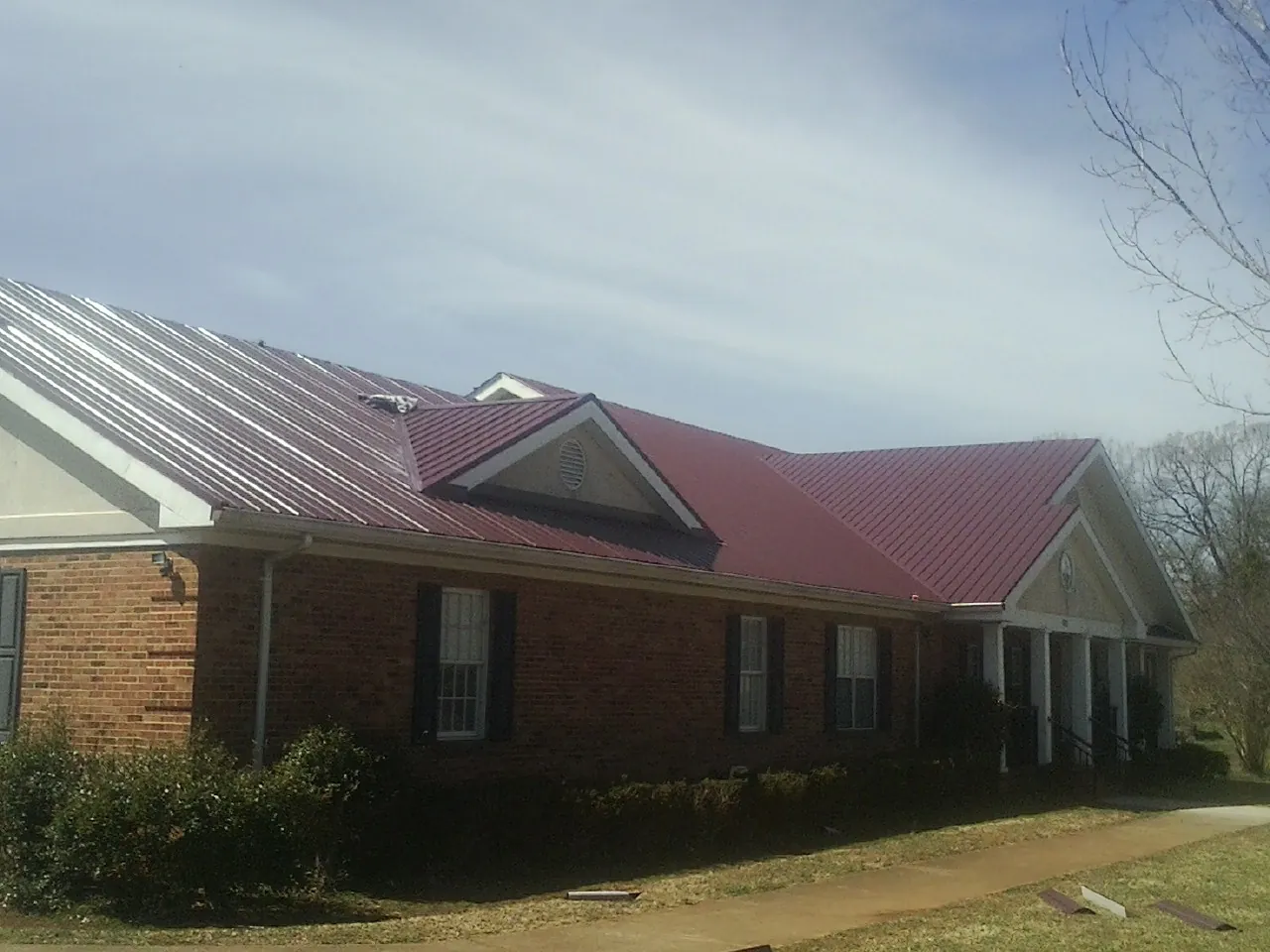Red metal roof with gabled entries on a long brick building, from a Hail Damage Roof Repair job in Whitefish