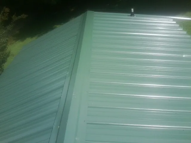 New green metal panels meeting at the ridge of a roof — Flat Roof Repair work by our crew in Whitefish