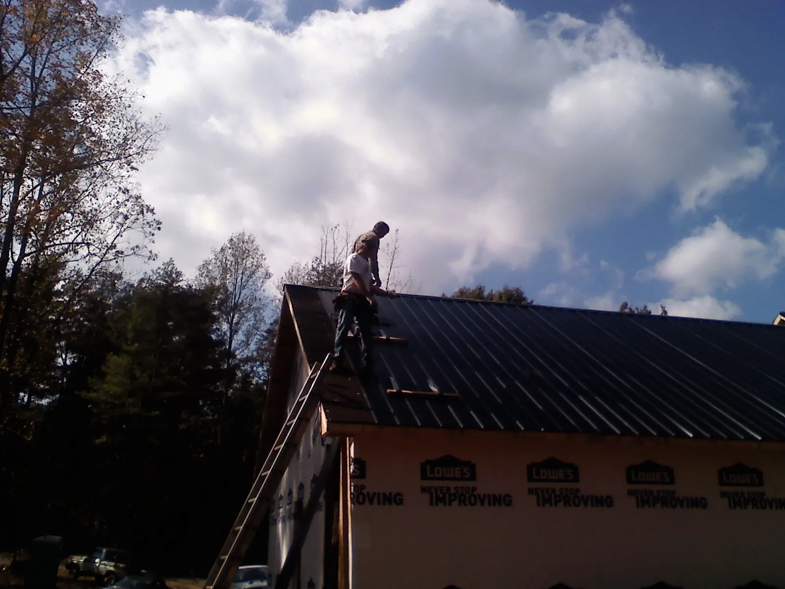 Roofer fastening dark metal panels high against a cloudy sky, from a Roof Inspection job in Whitefish