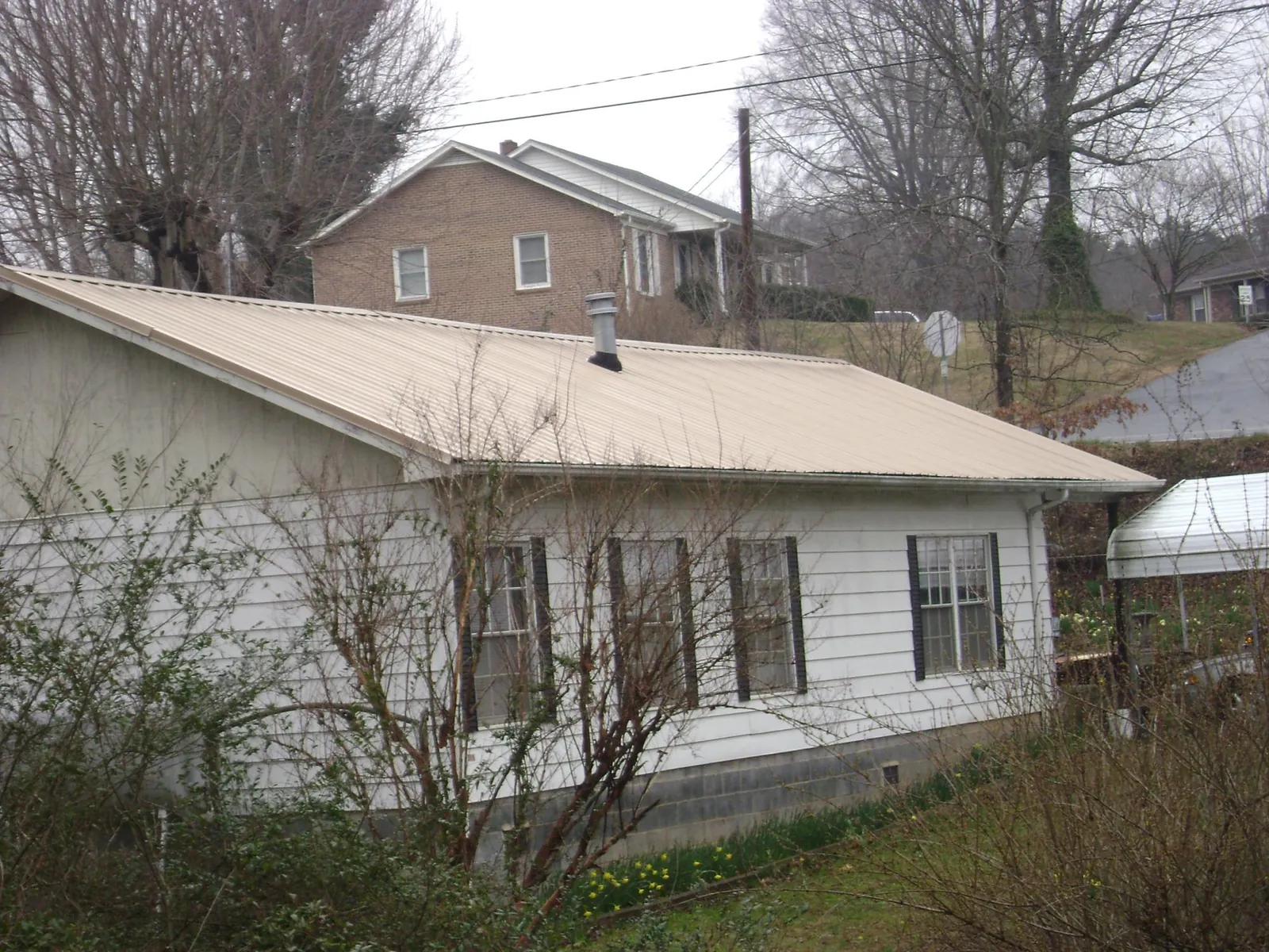 Tan metal roof on a white sided house set into a hillside — Commercial Roofing by Roofing Brothers in Whitefish