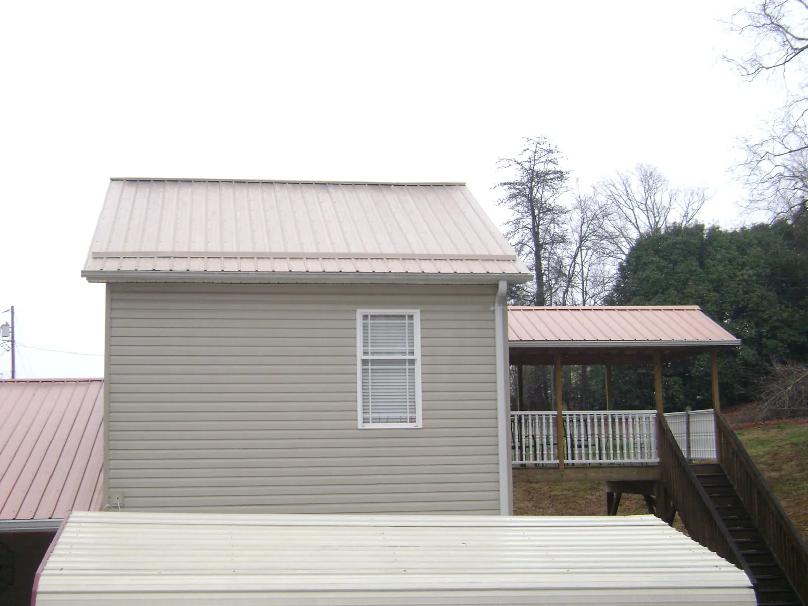 Tan metal roofs on a two story addition and attached porch, from a Roof Replacement job in Whitefish